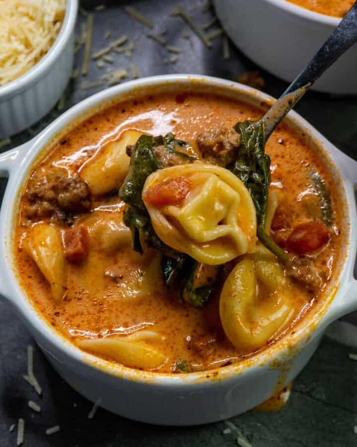 Close up of slow cooker creamy tortellini and sausage soup in a white bowl.