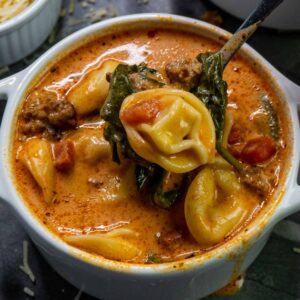 Close up of slow cooker creamy tortellini and sausage soup in a white bowl.