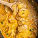 Cheesy scalloped potatoes in a slow cooker with a wooden spoon lifting some up.