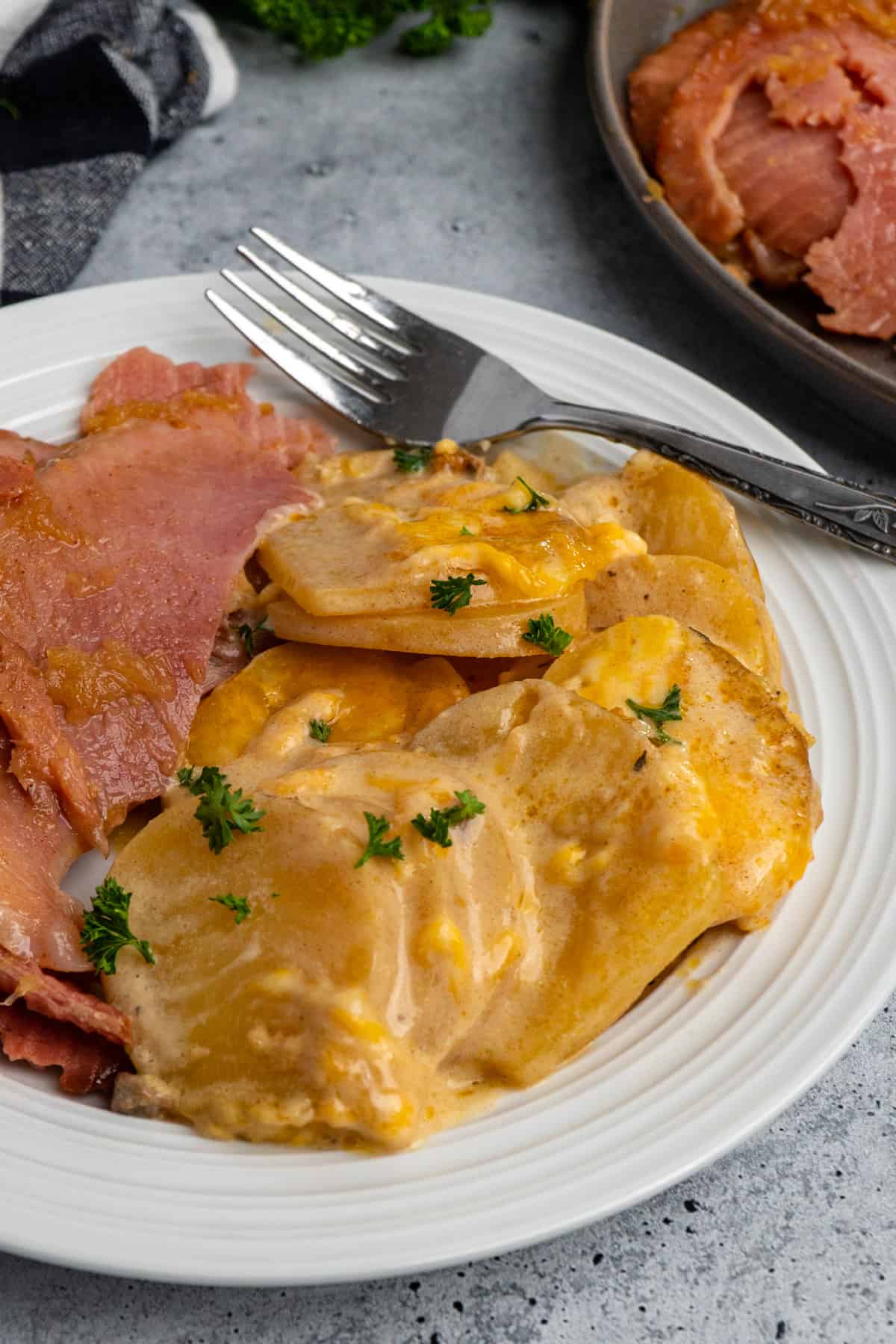 Scalloped potatoes on a white plate with slices of ham and a fork.