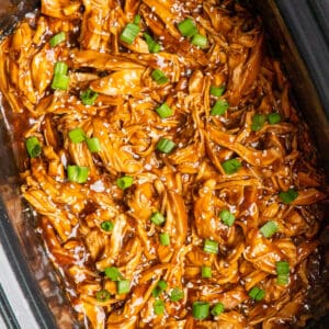 Close up of teriyaki chicken in a slow cooker garnished with sesame seeds and green onions.