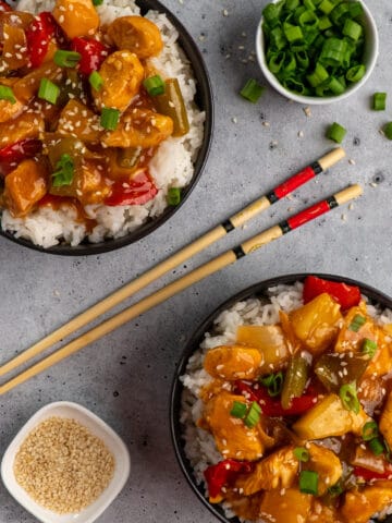 Two bowls of sweet and sour chicken over rice garnished with sesame seeds and green onions.