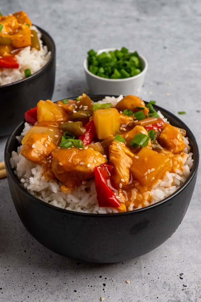 A bowl of Crock-pot sweet and sour chicken over rice with diced green onions in the background.