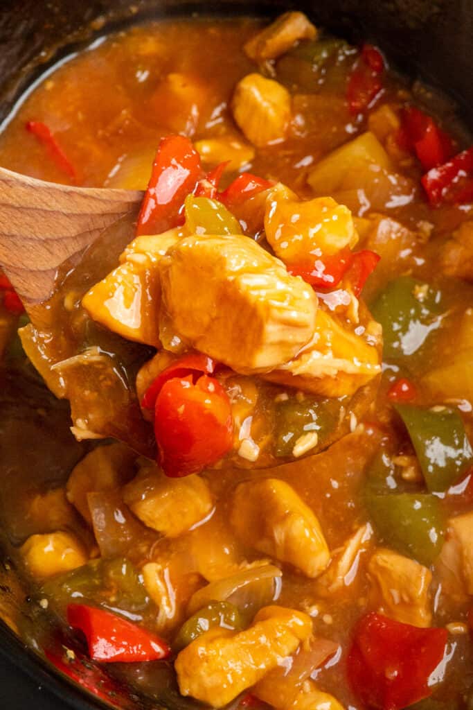 A wooden spoon full of Crock-Pot sweet and sour chicken over a slow cooker.