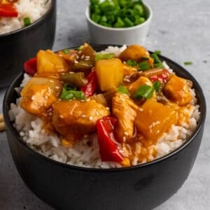 A bowl of Crock-Pot sweet and sour chicken over rice with diced green onions in the background.
