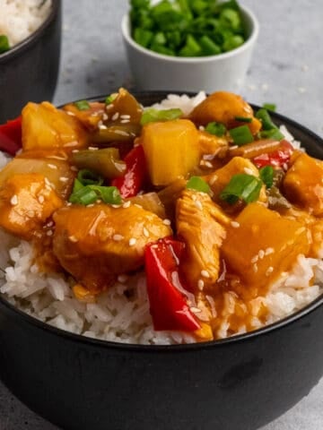 A bowl of Crock-Pot sweet and sour chicken over rice with diced green onions in the background.