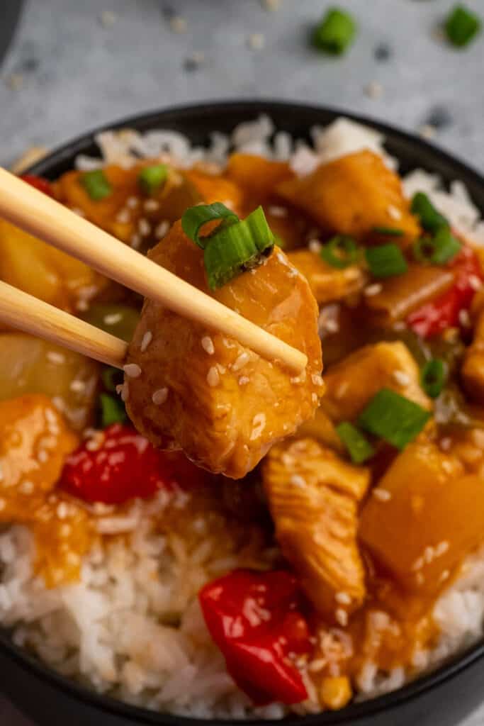 Close up of a piece of sweet and sour chicken being held by chop sticks.