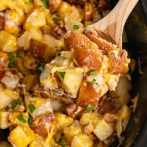 Close up of slow cooker cheesy bacon ranch potatoes on a wooden spoon.
