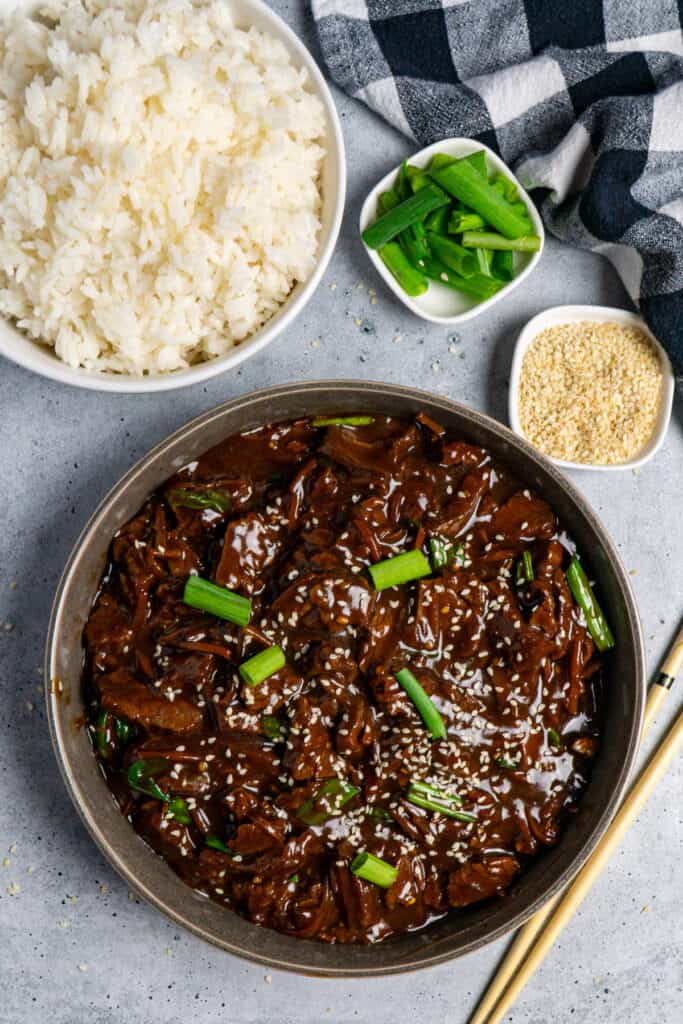 Slooker cooker Mongolian beef in a grey bowl topped with green onions and sesame seeds.