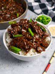 Close up of slow cooker Mongolian beef over rice and garnished with sesame seeds and green onions.