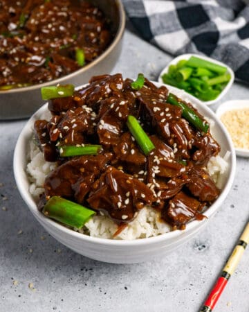 Close up of slow cooker Mongolian beef over rice and garnished with sesame seeds and green onions.