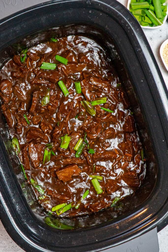 Mongolian beef in a Crock-Pot garnished with green onions.