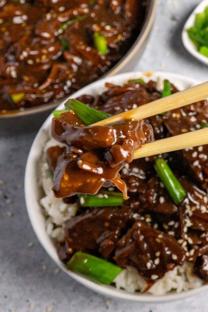 Close up of chop sticks holding a piece of slow cooker Mongolian beef.