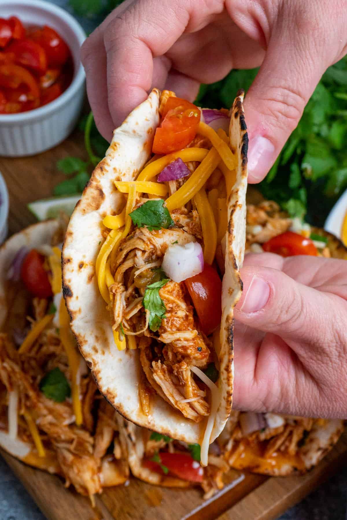 Two hands holding a shredded chicken taco up over a plate of more.