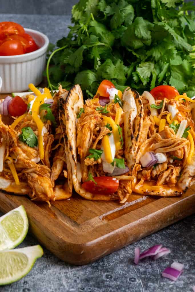 Close up of 3 slow cooker shredded chicken tacos on a wood cutting board.