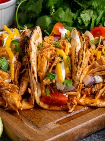 Three slow cooker shredded chicken tacos on a wood cutting board.