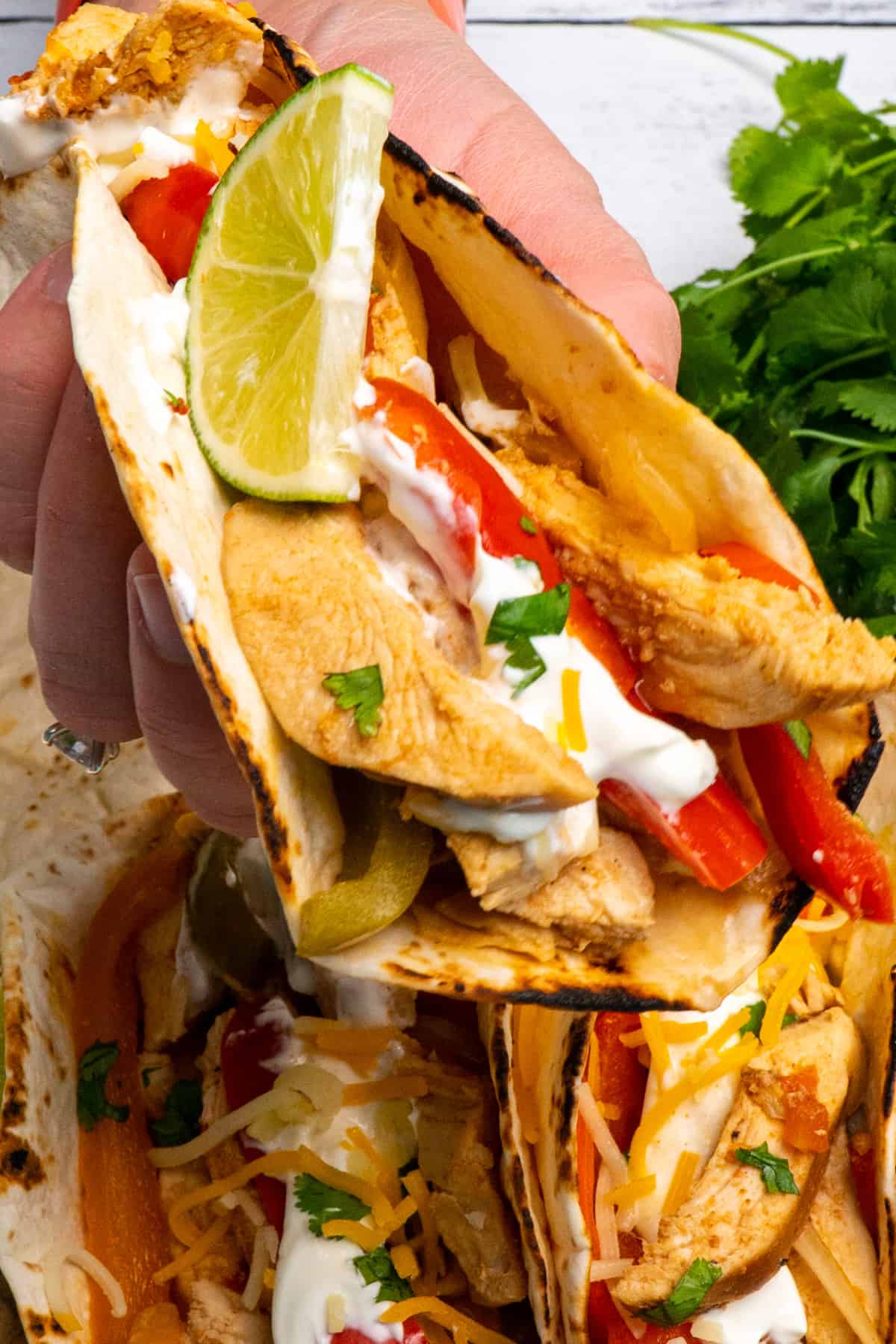Close up of chicken fajitas in a flour tortilla with a hand holding it.