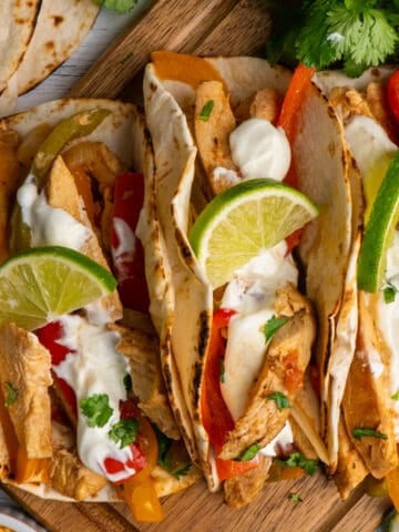 Crock Pot chicken fajitas in flour tortillas with fresh sliced limes on top.