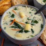 Close up of Crock-Pot chicken gnocchi soup in a grey bowl and bread in the background.