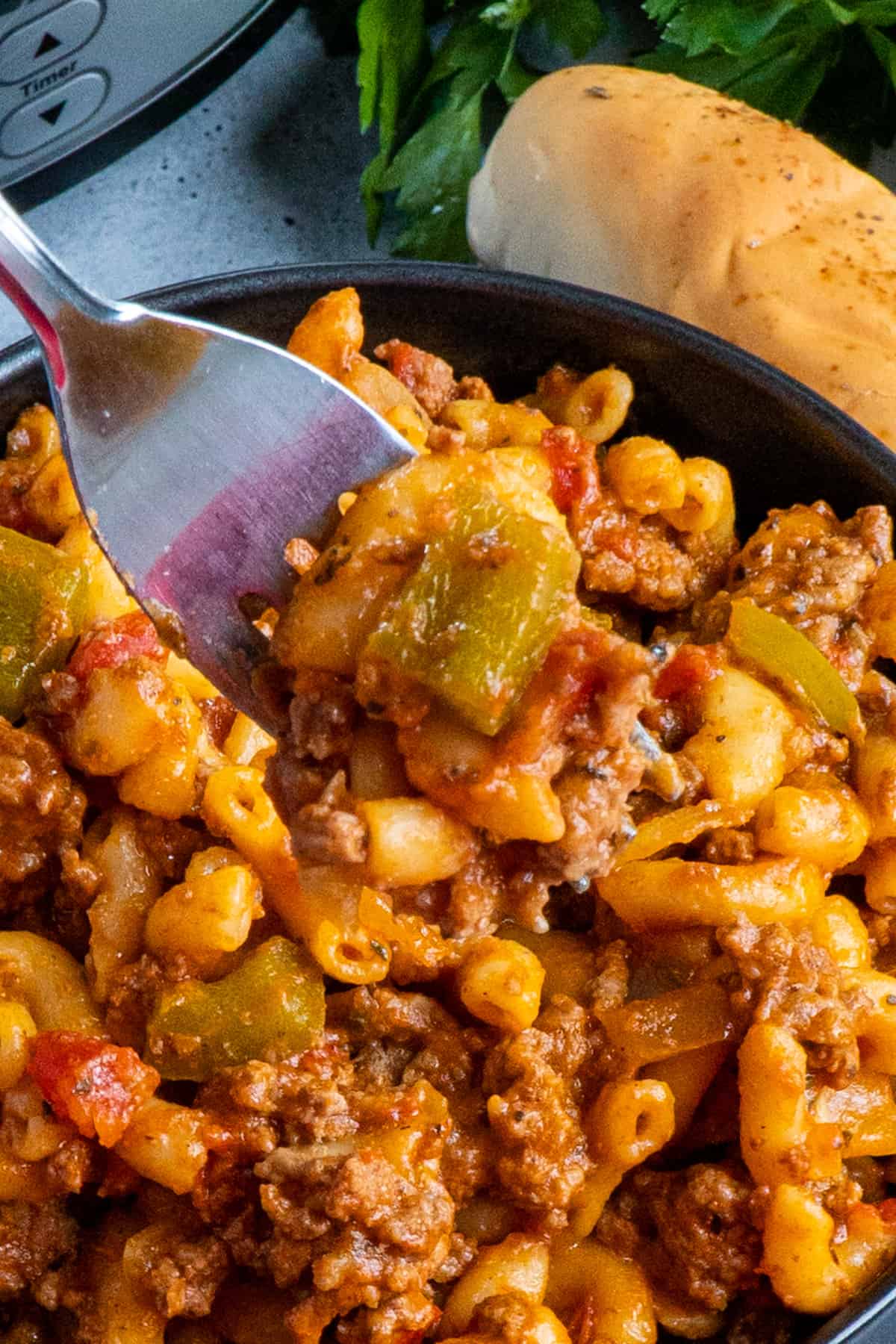 A fork holding a bite of goulash over a bowl.