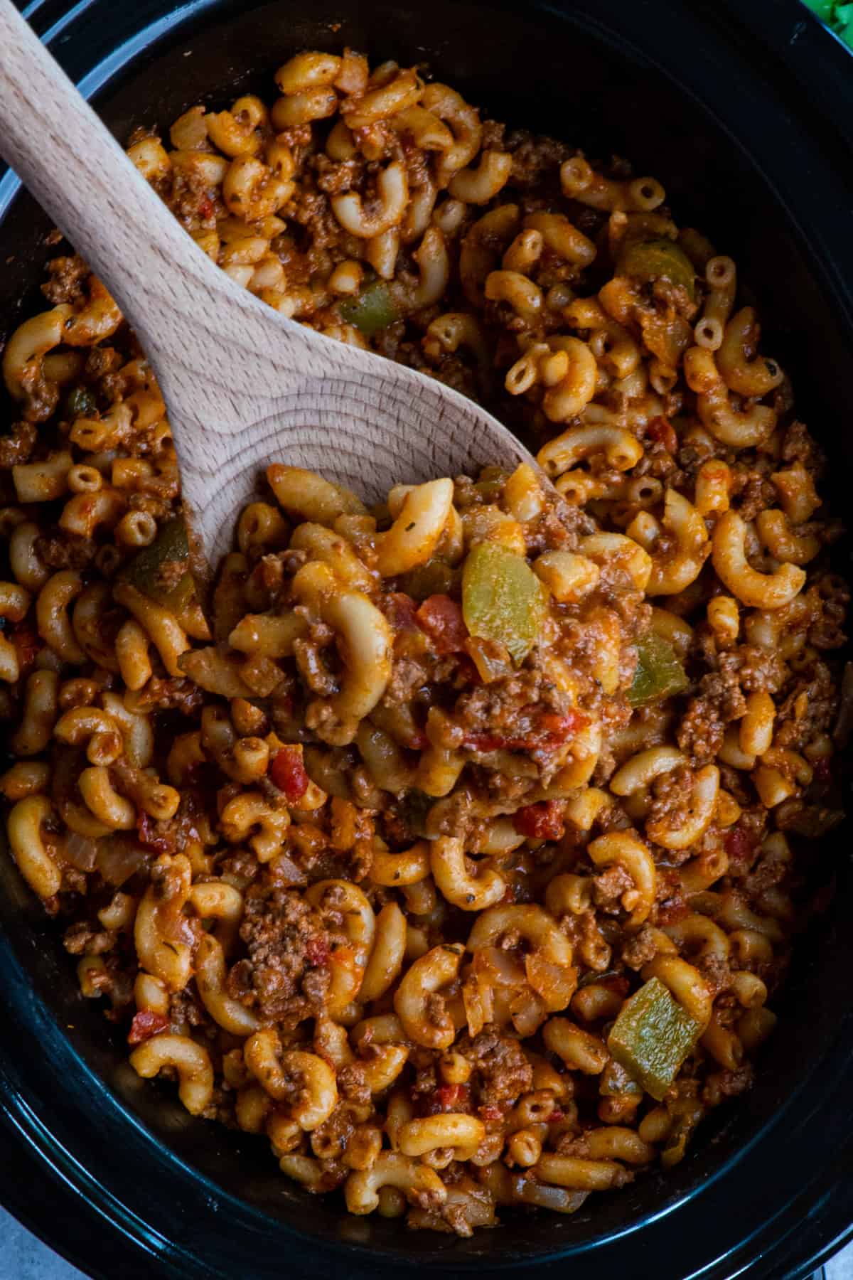 A wooden spoon holding a scoop of goulash over a crock pot.