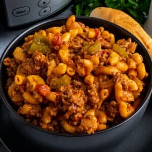 Crock Pot goulash in a black bowl and breadstick in the background.