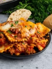 Close up of Crock-Pot lasagna with ravioli on a black plate and garnished with fresh parsley.