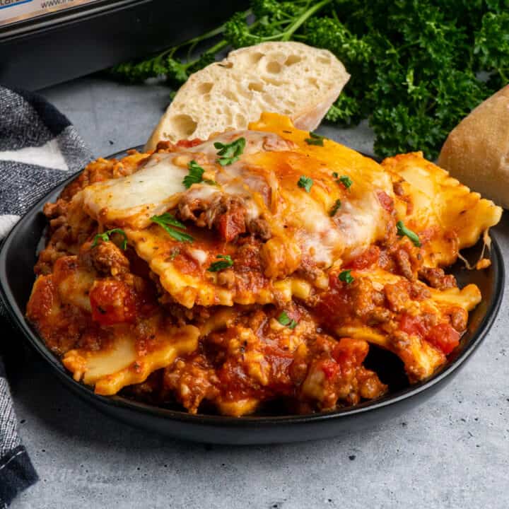 Close up of Crock-Pot lasagna with ravioli on a black plate and garnished with fresh parsley.