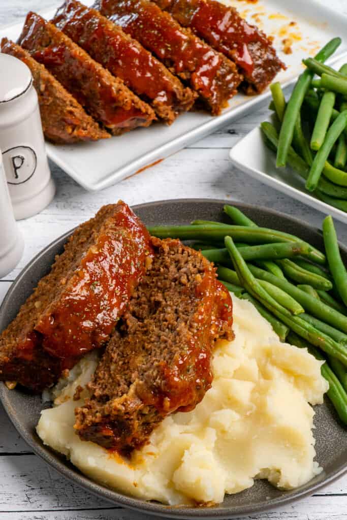 Crock-Pot Meatloaf with a glaze on top of mashed potatoes and a side of green beans.