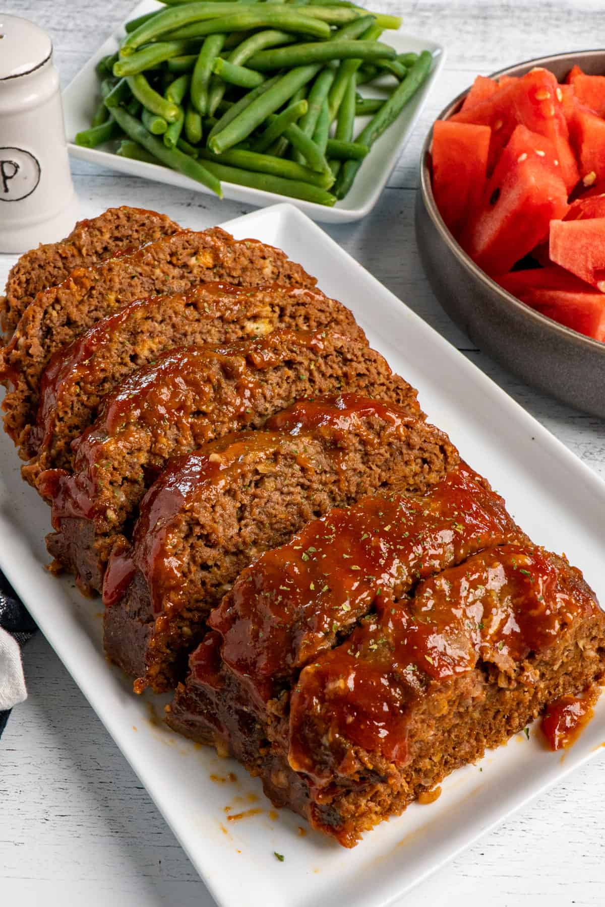 Close up of sliced meatloaf with a glaze on a white plate.