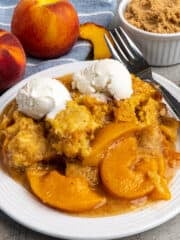 Close up of Crock-Pot peach cobbler on a white plate topped with ice cream.