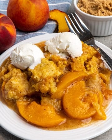 Close up of Crock-Pot peach cobbler on a white plate topped with ice cream.