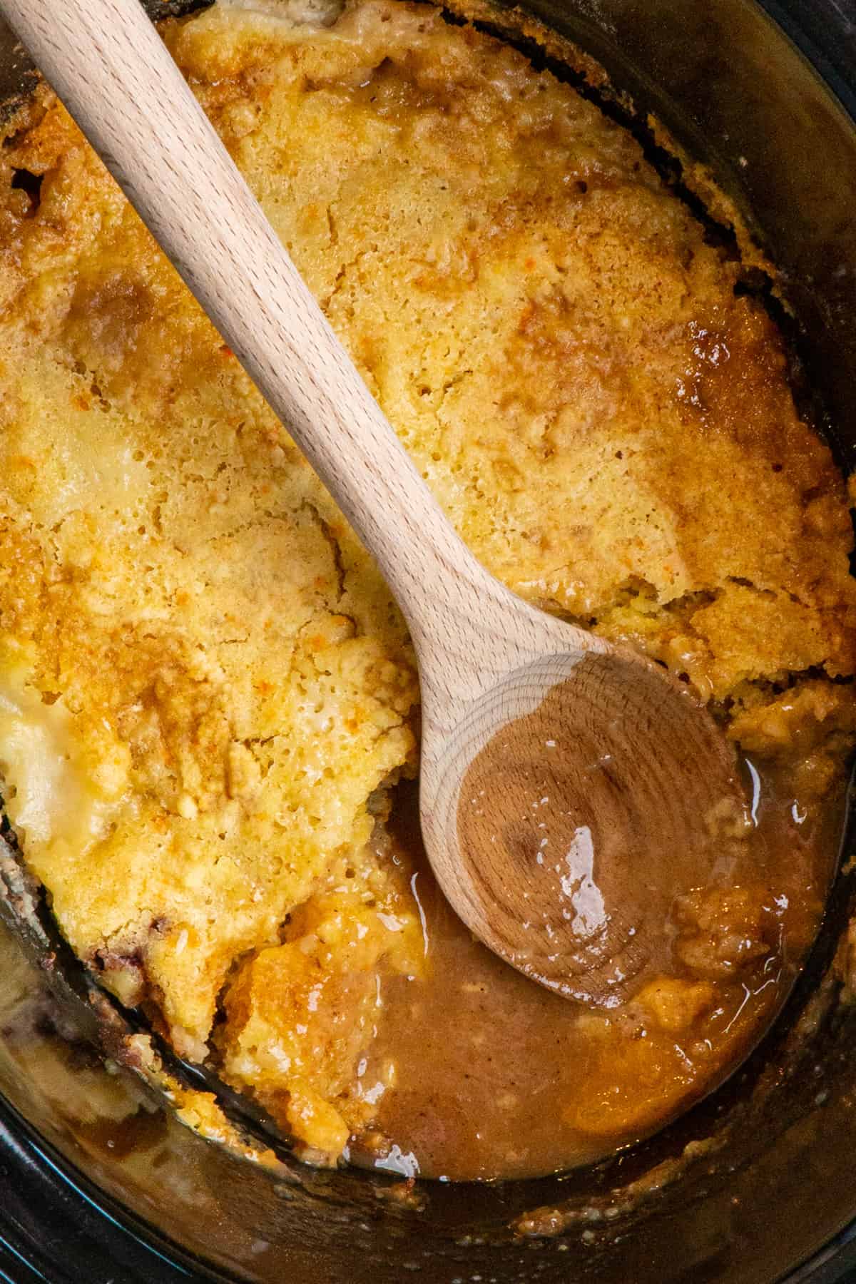 Peach cobbler in a slow cooker with a wooden spoon.