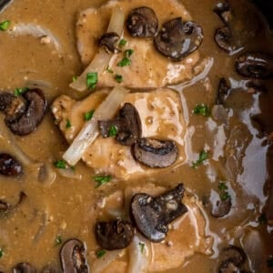 Close up of smothered pork chops in a Crock-pot with onions and mushrooms.