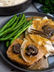 Crock-Pot smothered pork chops on a grey plate with green bean and mashed potatoes with gravy.