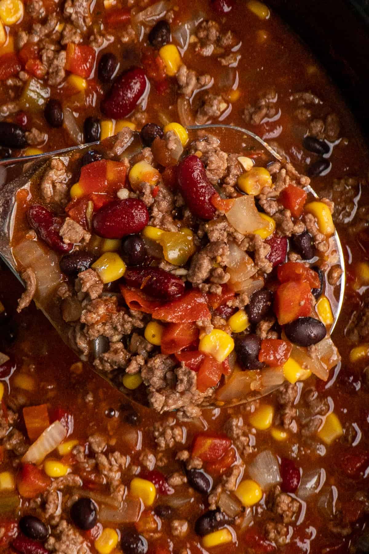 Taco soup in a ladle held up over a slow cooker to show off the ingredients.