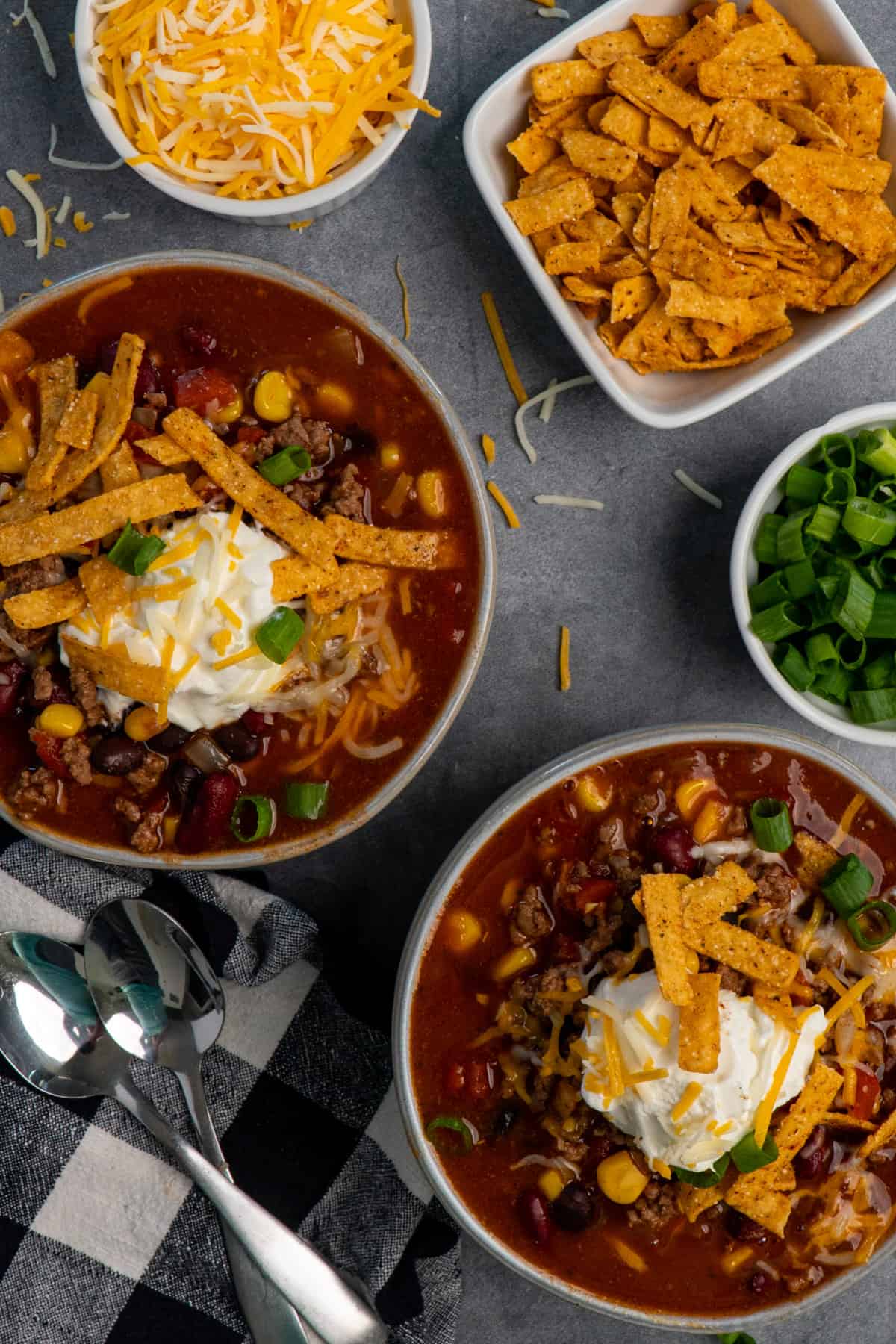 Two bowls of Crock-Pot taco soup topped with sour cream, green onions, cheese and tortilla strips on the table.