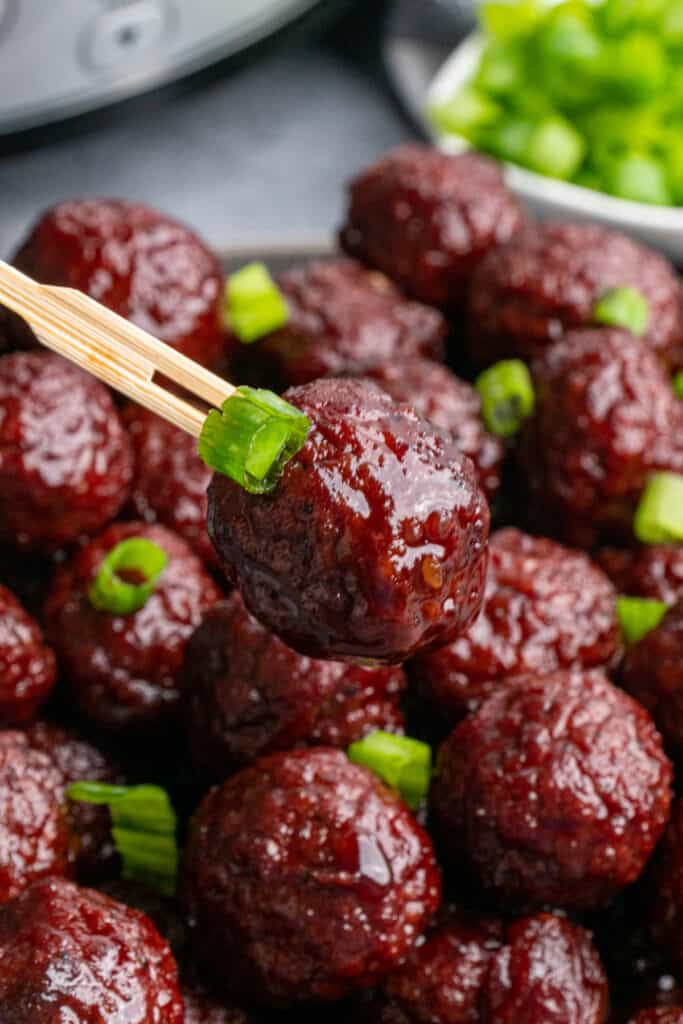Close up of a glazed meatball on a tooth pick and garnished with green onions.