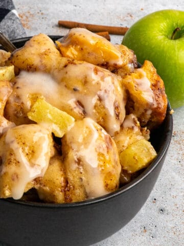 Close up of slow cooker apple cinnamon rolls in a black bowl.