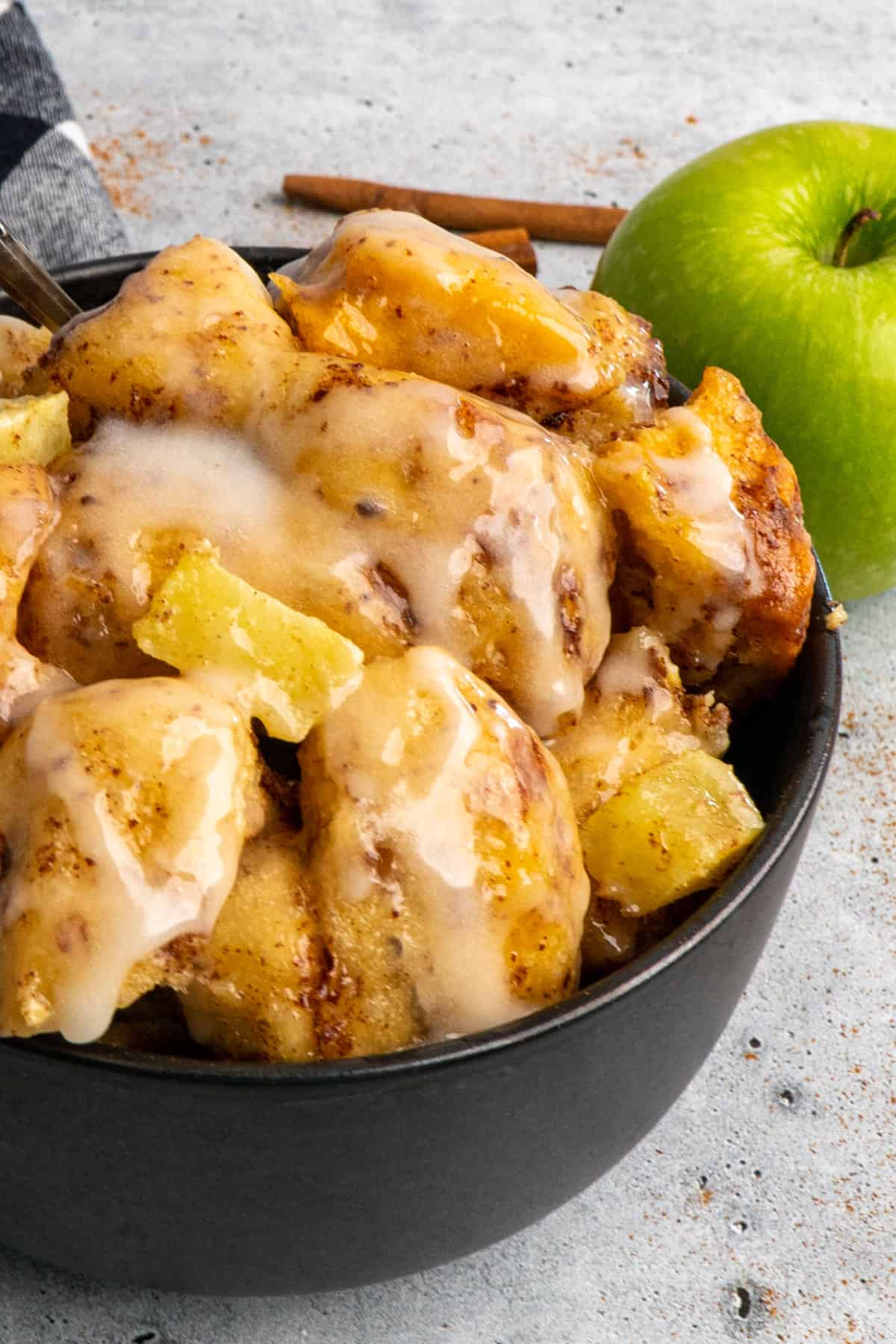 Close up of apple cinnamon rolls in a bowl with a green apple next to it.