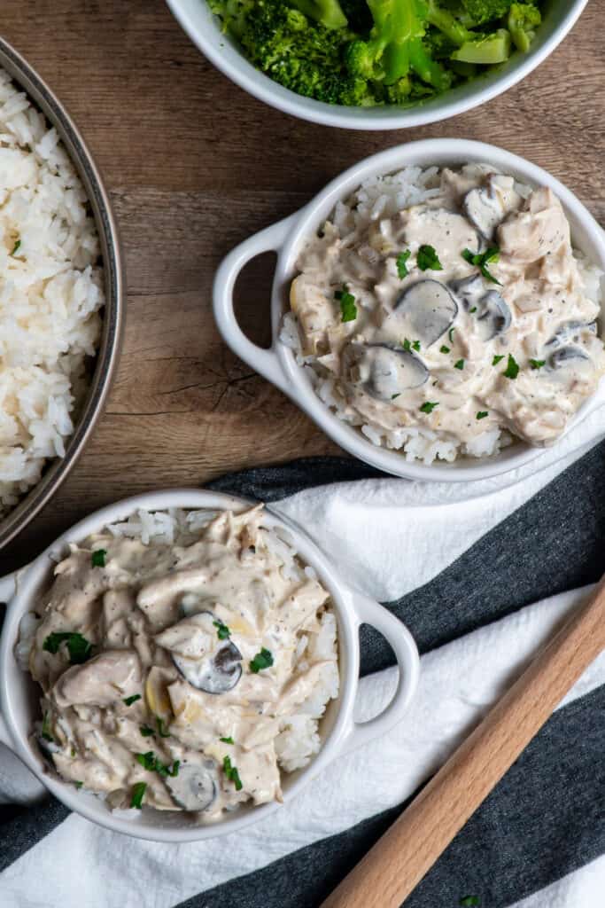 Two bowls of artichoke mushroom chicken over rice and garnished with fresh parsley.