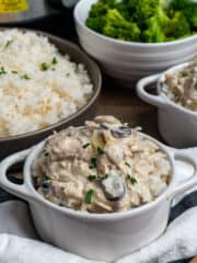 Slow cooker artichoke mushroom chicken in a white bowl over rice and broccoli in the background.