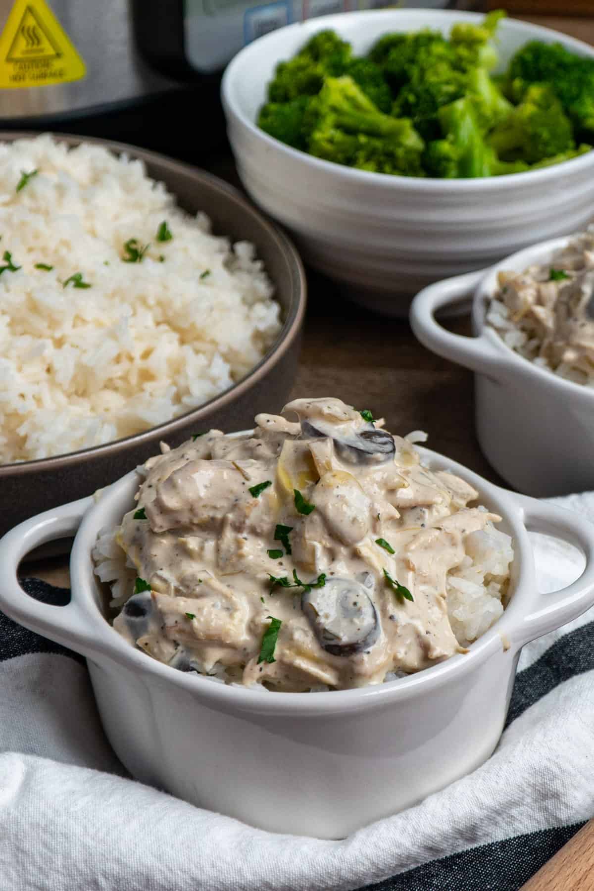 Slow cooker artichoke mushroom chicken over rice in a white bowl.