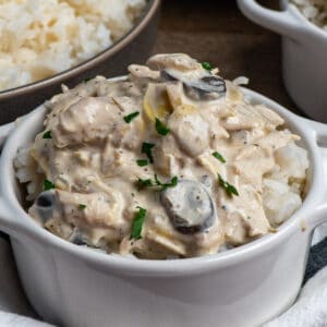 Close up of slow cooker artichoke mushroom chicken in a white bowl over rice.