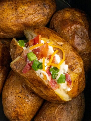 Close up of a loaded baked potato in a slow cooker on top of other potatoes.