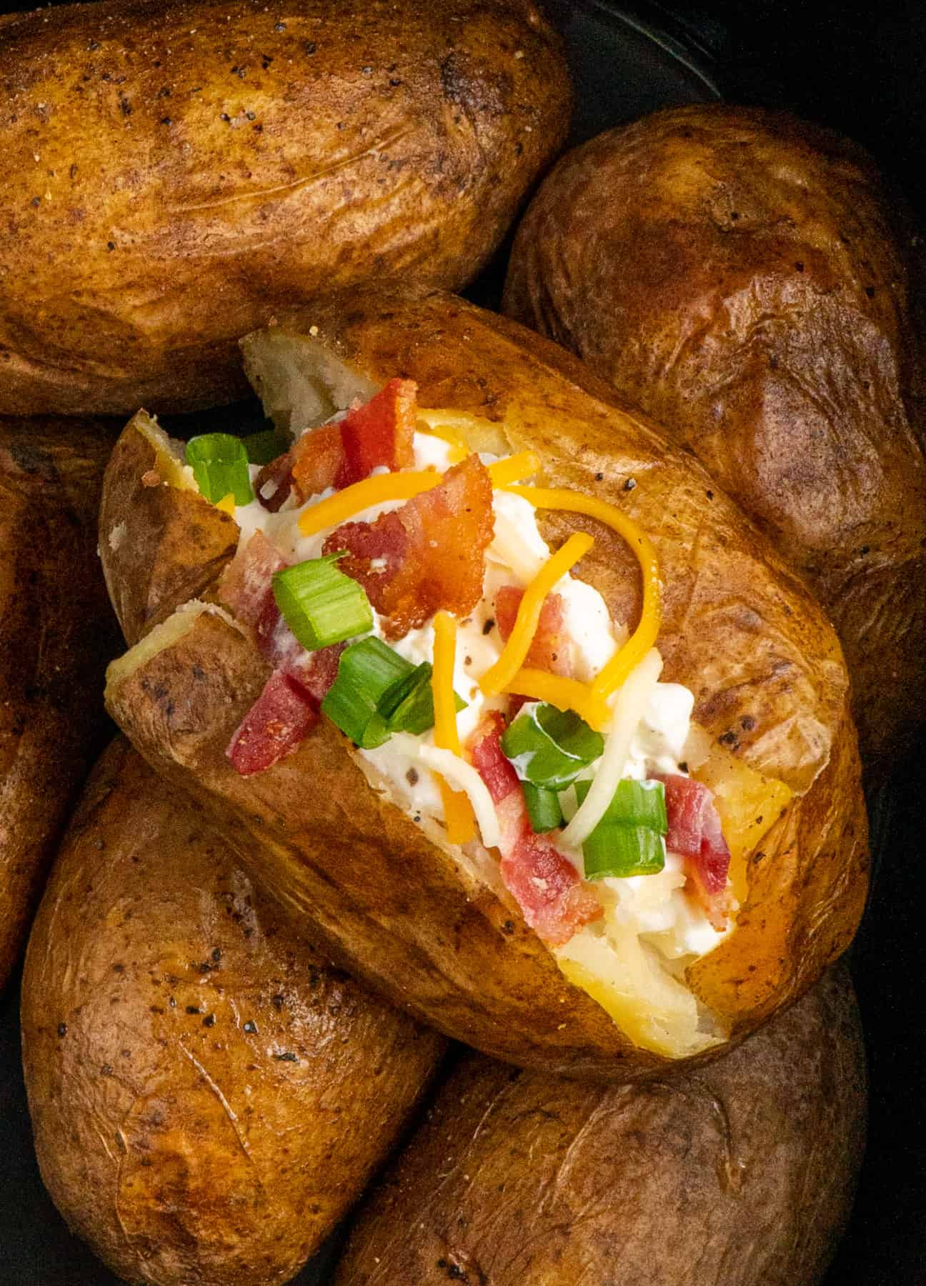 Close up of a loaded baked potato in a slow cooker on top of other baked potatoes 