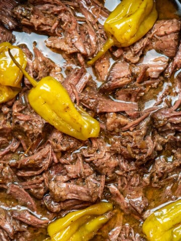 Close up of Mississippi pot roast in a slow cooker with pepperchinis on top.
