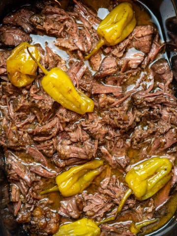 Close up of Mississippi pot roast in a slow cooker with pepperchinis on top.