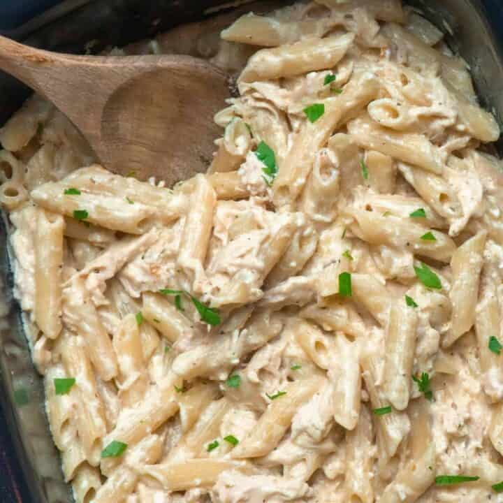 Olive Garden chicken pasta in a crock pot garnished with fresh chopped parsley.