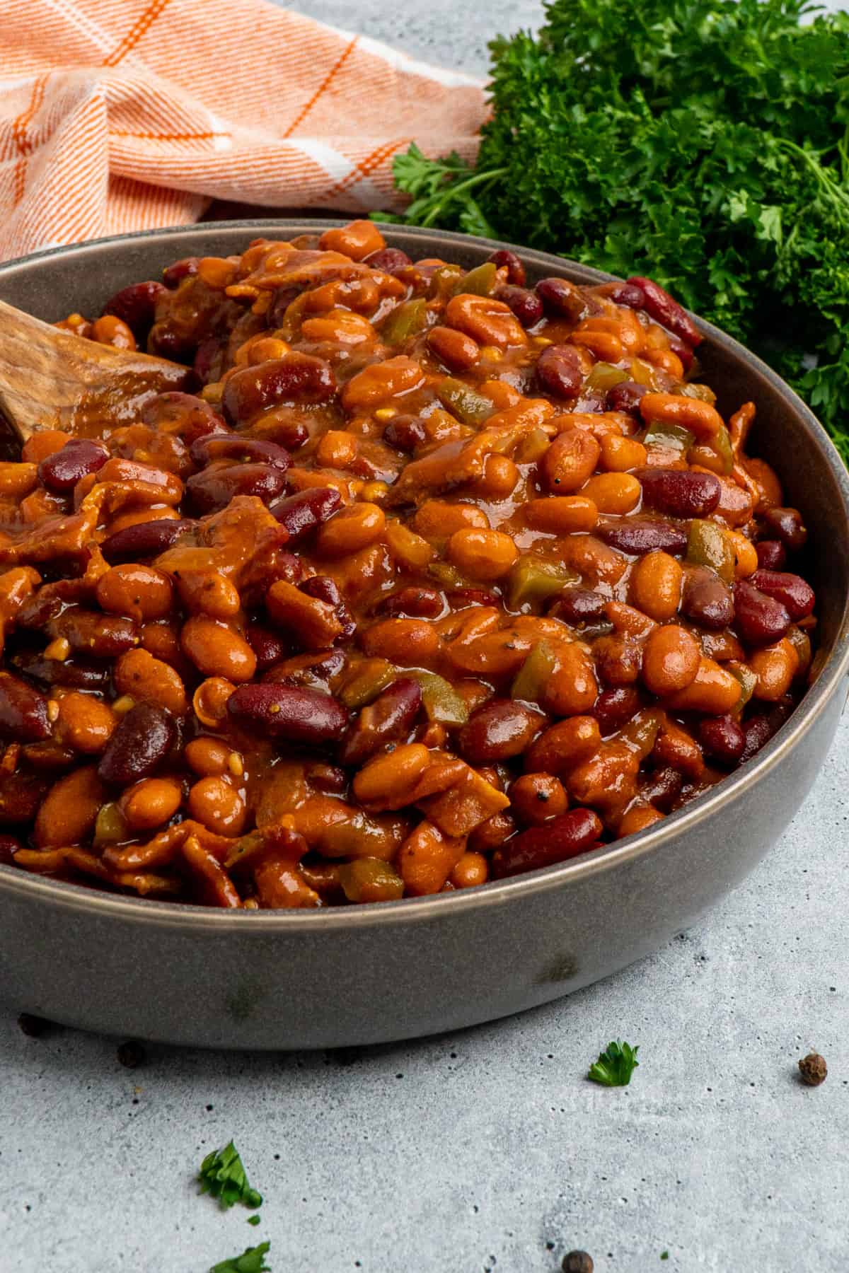 Close up of crock pot baked beans in a grey bowl with a wooden spoon in it.